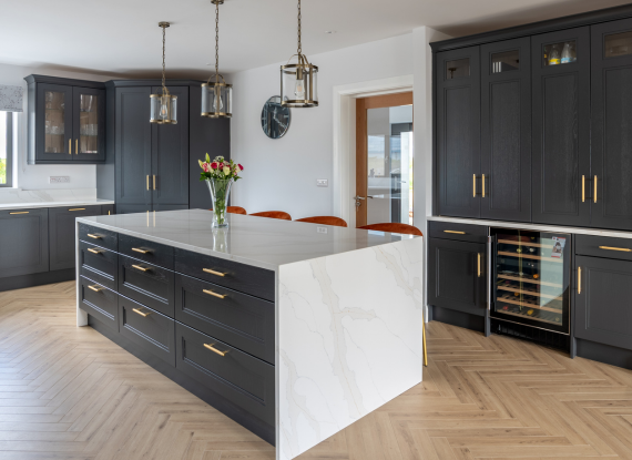 2._A Darker Palette Balanced with Warmth The Quartz Calacatta Gold waterfall island introduces warmth and movement through its softer gold veining, while the contrasting Neolith Himalayan Crystal backsplash creates a cleaner and more modern finish around the cooking zone. Using two different stone surfaces allows key areas of the kitchen to feel more layered, balanced, and visually defined.